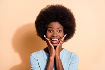 Photo portrait of amazed african american woman smiling touching face with hands isolated on pastel beige colored background