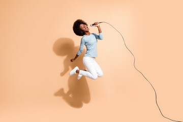 Photo portrait of crazy african american girl holding microphone in one hand singing in air isolated on pastel beige colored background