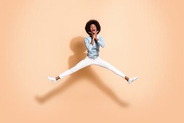 Fototapeta na wymiar Photo portrait of black skinned woman holding two hands near face jumping up with spread legs open mouth isolated on pastel beige colored background