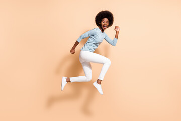 Fototapeta na wymiar Full length body size side profile photo of funny dark skinned curly girl jumping high running fast laughing loudly isolated on beige color background