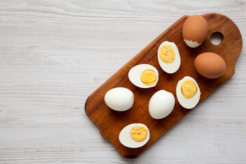 Hard Boiled Eggs on a rustic wooden board on a white wooden background, top view. Flat lay, overhead, from above. Space for text.