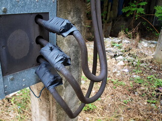 Cables or wires with close couplings. Electrical connection points on the side of the control box and wrapped in black insulating tape. On the ground background and green trees. Selective focus