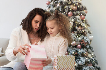 Family christmas morning. Mom and daughter open gifts. Girls greet Christmas among boxes of gifts and Christmas lights.