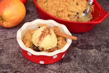 Apple crumble dessert with cinnamon and vanilla ice cream on dark background