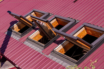 Opened roof windows. Skylight on red ceramic house tiles. Skylights windows, sun tunnels. Building construction, installation of metal-plastic structures.