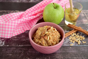 Hot breakfast oat porridge with apple, hazelnuts, honey and cinnamon powder  on a wooden rustic background.