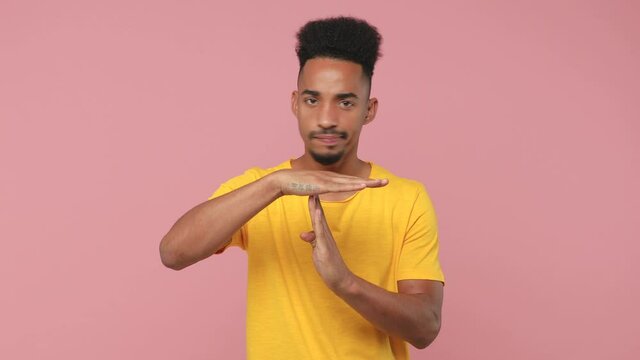 Displeased concerned young african american man 20s years old in yellow t-shirt posing isolated on pastel pink background studio. People lifestyle concept. Looking camera holding hands perpendicularly