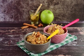 Hot autumn breakfast oat porridge with apple, hazelnuts, honey and cinnamon powder on a wooden rustic background.