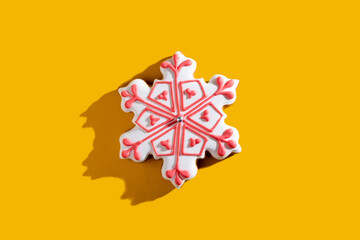 Christmas food decor. Festive pastry. New Year sweet ornament. White homemade gingerbread snowflake with pink icing isolated on orange copy space background.