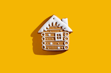 Christmas biscuit. Festive bakery food. Winter holidays ornament. Beige gingerbread house cookie with white snow icing creative decoration isolated on yellow copy space background.