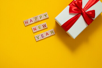 Happy New Year and Merry Christmas. Scrabble letters with holiday present on yellow background. Letter tiles spelling celebration holiday.