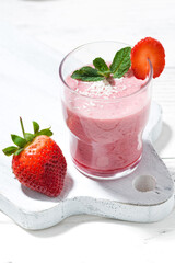 glass of refreshing strawberry milkshake on white table, closeup