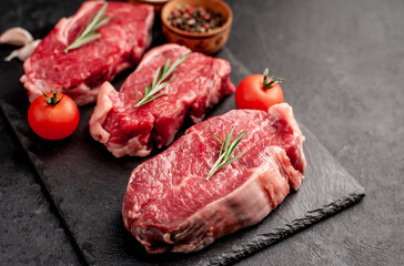raw three beef steaks on a cutting board with spices on a stone background