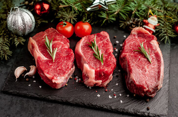 Three raw beef steaks with spices for Christmas with toys and a Christmas tree on a stone background