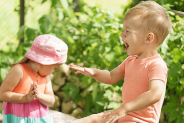 Summer, vacation, childhood, communication concepts. Two children of the same age show different emotions. Children in the garden play outdoors in summer. happy little surprised boy sitting on a stump