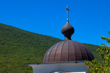 Dome of the Orthodox Church with a gilded cross against the background of green mountains and blue...