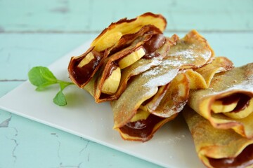 Crepes with chocolate and banana garnish with mint leaf and powdered sugar