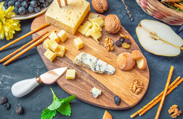 Cheese plate from different kind of cheese - Emmental, Homemade, Parmesan, blue cheese, bread sticks, walnuts, raisin, pear, grapes on a table