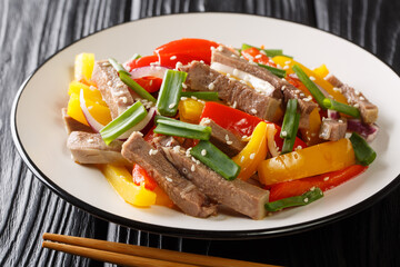 Delicious warm salad of beef tongue with bell pepper, onion and sesame seeds close-up in a plate on the table. horizontal