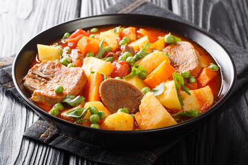 Cooked beef tongue with vegetables in tomato sauce close-up in a bowl on the table. horizontal