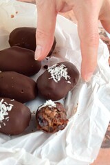 A hand picking Medjool dates covered dark chocolate garnish with shredded coconut