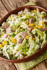 Beef tongue salad with fresh cabbage, corn and onions close-up in a bowl on the table. vertical