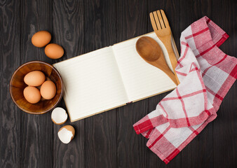 Recipe Cooking book, Wooden kitchen Utensils, eggs and flour on dark rustic wooden background.