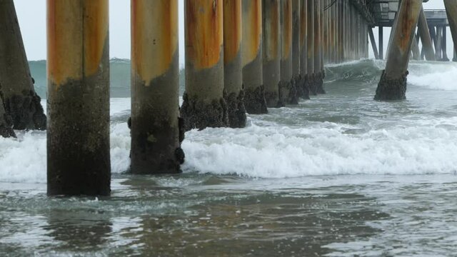 Waves coming in under a pier on an overcast day slow motion