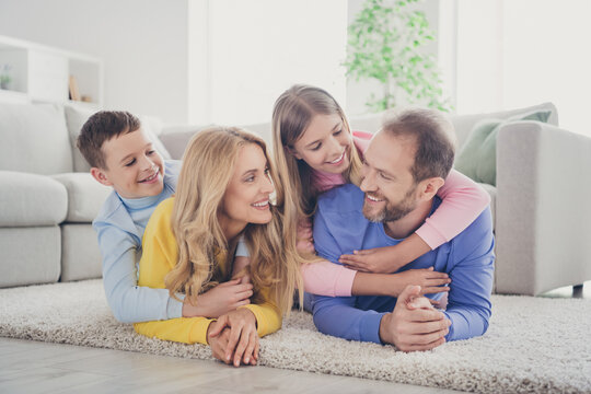 Photo of charming mom dad lying carpet hold piggyback two adorable little kids girl boy in house indoors