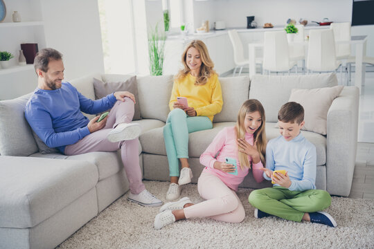 Full size photo of family people mom dad two small kids sit floor sofa read social network shocked news in house indoors