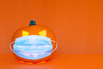 Safe Halloween 2020 during Covid-19 pandemc. Halloween carved luminous pumpkin with face mask orange wall studio shot