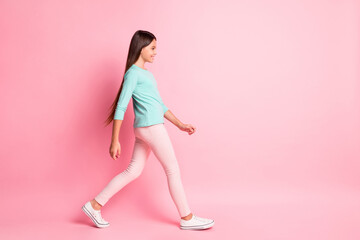 Full body size profile photo of lovely sweet small latin lady long hairdo walk look empty space smile wear turquoise sweatshirt pants white sneakers isolated pink color background