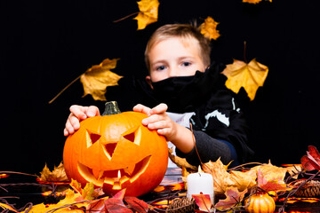 young boy in costume dressed as a halloween cosplay of scary dacula holding a jack'o pumpkin lantern