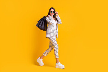 Fototapeta na wymiar Full length body size photo of happy girl keeping black friday shopping bags touching sunglass isolated on bright color background
