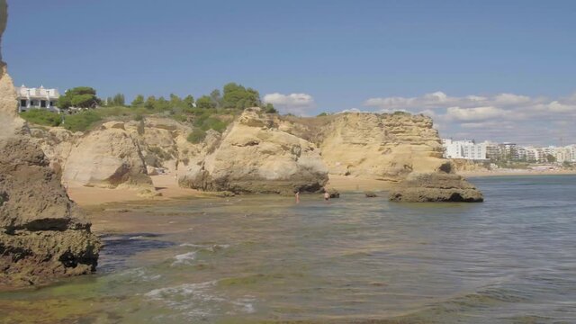 Drone flies low around Sea Cliff with luxury white hotel with palm trees perched up on top and people in water