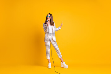 Full length body size photo of woman keeping mic singing pop song smiling wearing sunglass isolated on bright yellow color background