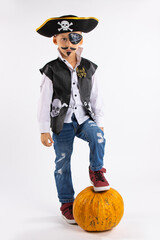 Halloween holiday. Little boy in a pirate costume and with a huge pumpkin in full growth, looking...
