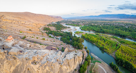 Wide panorama view of  Mtkvari river surounded by green nature and Uplistsiche cave town rock formations. Travel in scenic places. Georgia.