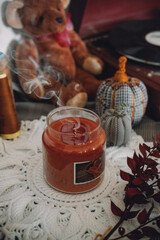 Winter cozy mood concept. Still life details in home interior of living room. Scented Soy Aromatherapy Candle and cup of tea with steam on table. Cozy autumn or winter concept