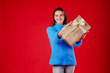 girl in a blue sweater holding a gift in her hands on a red background.