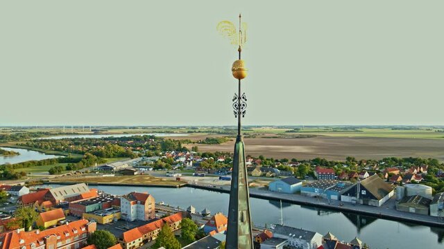 Tall spire on a large medieval church made from red bricks. Spire features a golden weathercock and panoramic view over an old European town. 4K aerial video.