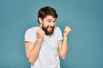 Fototapeta premium A bearded man in a white T-shirt gestures with his hands emotions blue background