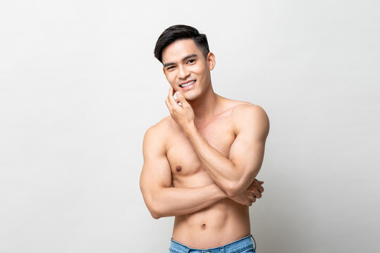 Portrait of shirtless handsome Asian man smiling and touching his face in light gray isolated studio background