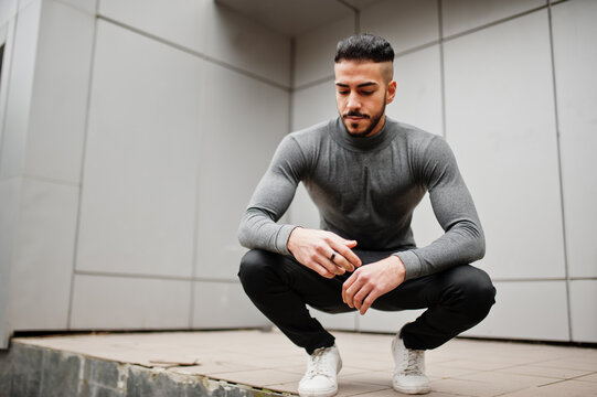 Portrait of stylish arab beard man wear grey turtleneck. Arabian model guy against steel wall squat.