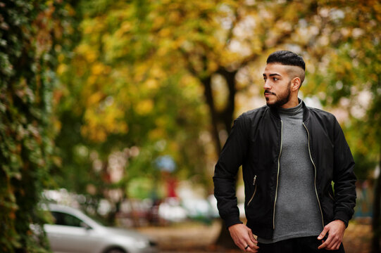 Portrait of stylish arab beard man wear grey turtleneck and black jaket. Arabian model guy on a background of autumn leaves.
