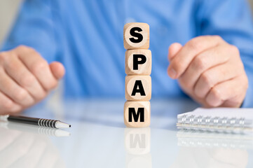 Geschäftsmann mit Würfeln auf denen SPAM steht am Schreibtisch mit Stift und Block