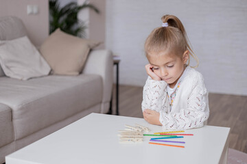 Naklejka premium Little girl sitting at the table and think about math exercise.