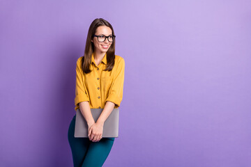 Photo of charming girl hold pc look side empty space wear specs yellow shirt blue pants isolated...