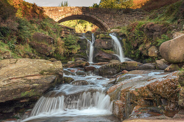 Three Shire Heads. An autumnal waterfall and stone packhorse bridge at Three Shires Head in the Peak District.