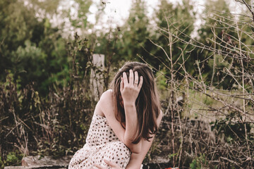 very upset girl covered her face with her hands, sat down on a background of dry trees and nature © Марина Шемедюк